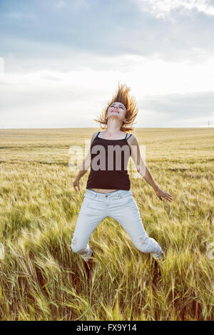 Crazy caucasian woman is jumping in the wheat field and makes big fun. Beauty and nature. Stock Photo