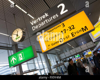 Signs, clock and travellers in departure terminal of Schiphol Amsterdam Airport, Netherlands Stock Photo