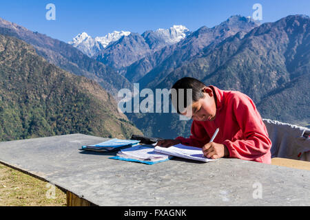 A schoolboy doing his homework outside, high mountains in the distance, Sibuje, Solo Khumbu, Nepal Stock Photo