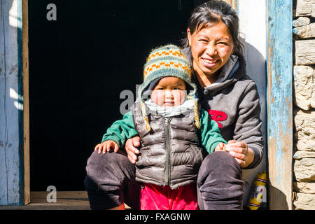 Portrait of a smiling young nepali mother with her child sitting in a doorway, Chheplung, Solo Khumbu, Nepal Stock Photo