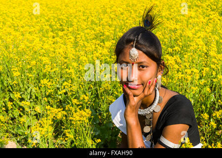 Portrait of a young local woman belonging to the Tharu tribe, sitting in a yellow mustard field, Sauraha, Chitwan, Nepal Stock Photo