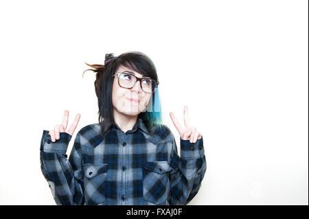 Smiling alternative teen woman in blue shirt looking up her left isolated doing victory sign with finger Stock Photo