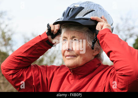 Active elderly senior retired woman putting on a bike cycling helmet preparing to go for a cycle ride to keep fit healthy in retirement. England UK Stock Photo