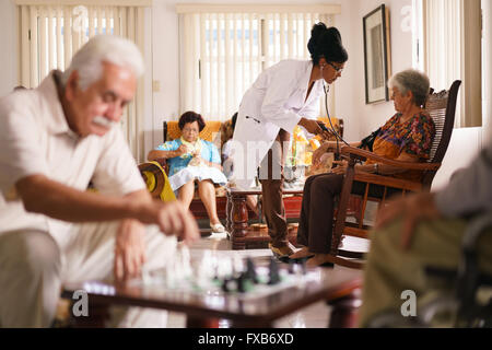 Old people in geriatric hospice: Black doctor visiting an aged patient, measuring blood pressure of a senior woman. Group of ret Stock Photo