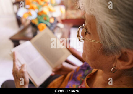 Old people in geriatric hospice: senior woman with eyeglasses and miopia problems sitting on chair and reading a book. Stock Photo