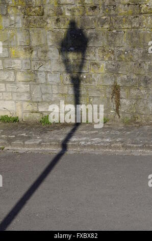Shadow of a street lantern on a street and stone wall next to it Stock Photo