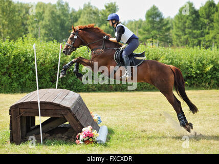 Young woman and her horse jumping log on cross country course at equine event Stock Photo