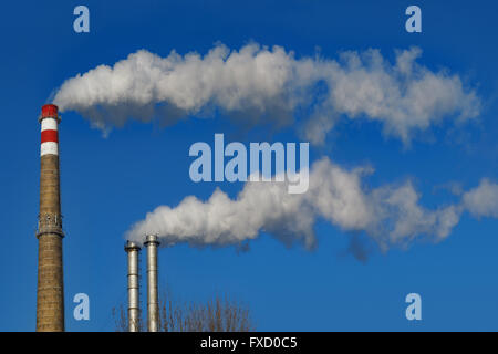 Chimneys smoke.  Pipes emits long trail of smoke on blue sky background. Stock Photo
