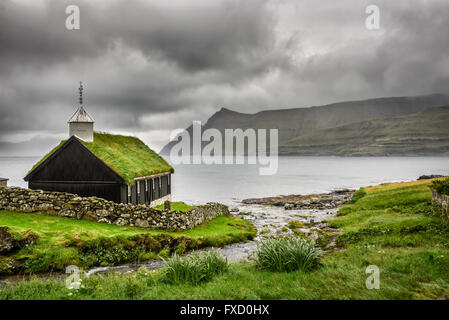 Small village church in Funningur under heavy clouds. Funningur is located on the island of Eysturoy, Faroe Islands, Denmark Stock Photo