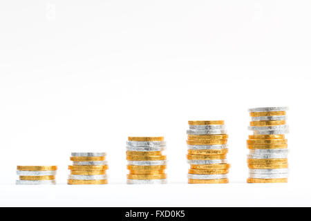 Columns and rows of gold and silver coins in the shape of an upward growth graph and on an isolated white background.