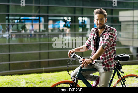 Handsome young man riding his bike in front of a glass building Stock Photo