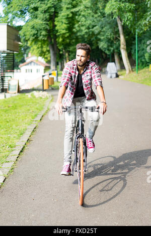 Handsome young man with blue eyes on his bicycle in an alley of trees , looking at the camera and enjoyng spring Stock Photo