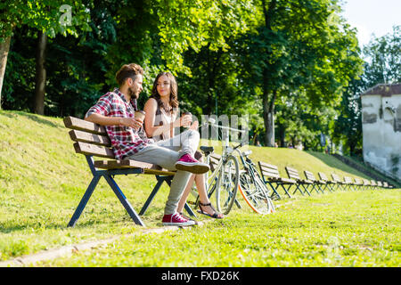 sweet friends having coffee under the sun in park, having bikes close by. Stock Photo