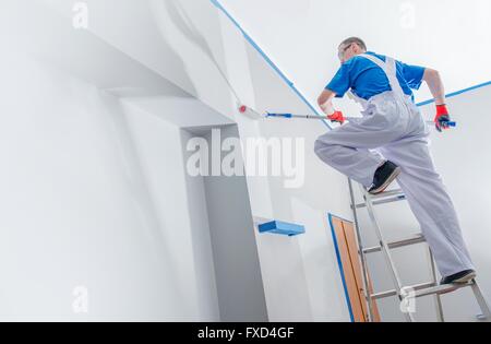 House Painting and Renovation Business Concept. Caucasian Male Painting House Room From the Ladder. Stock Photo