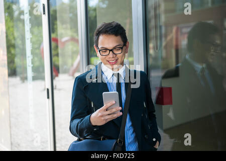 Young asian business man looking at mobile phone outside on city street near building Stock Photo