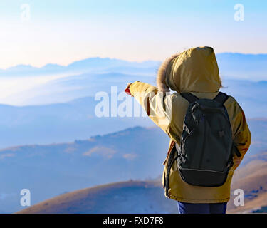 young Explorer with Backpack admires the panorama from the top of a mountain in winter Stock Photo