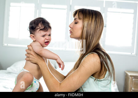Mother holding crying son on bed at home Stock Photo