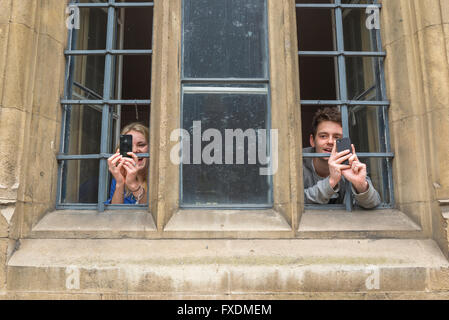 Couple taking photo, view of two Cambridge university students in Trinity College taking photos from an upstairs window, Cambridge, UK Stock Photo