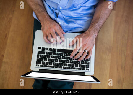 Mid-section of man sitting on floor and using laptop Stock Photo