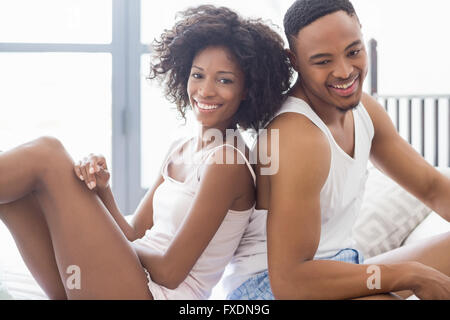 Happy young couple sitting back to back on bed Stock Photo
