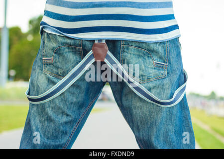 Fashion. closeup young fashionable man casual style wearing denim pants with suspenders back view outdoor Stock Photo