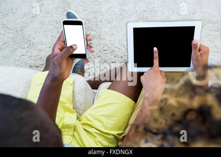 Couple using digital tablet and mobile phone in living room Stock Photo