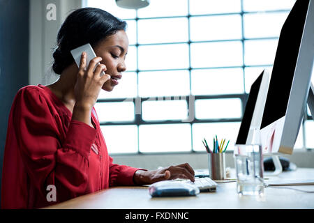 Woman talking on phone while using computer in office Stock Photo