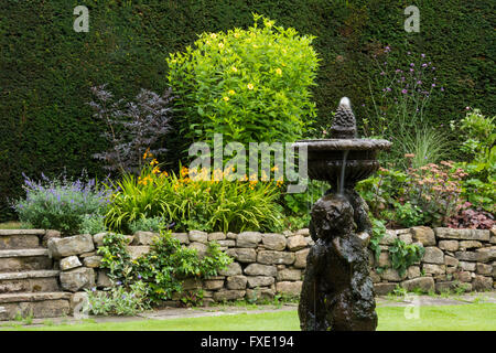 A beautiful, private, traditional, landscaped, country garden, West Yorkshire, England  - ornamental cherub fountain, stone wall and flower border. Stock Photo