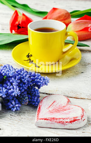 Yellow cup with tea,symbolic of the heart and a bouquet of red tulips Stock Photo