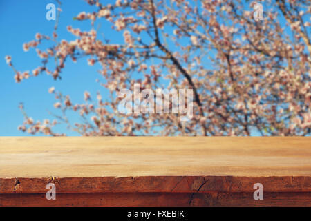 wooden rustic table in front of spring white cherry blossoms tree. vintage filtered image. product display and picnic concept Stock Photo