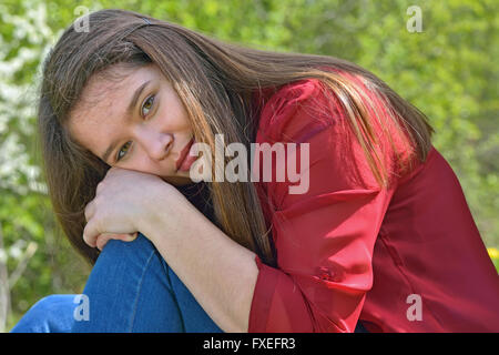 Teen girl sits hugging her knees outdoors Stock Photo
