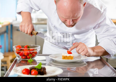 Professional chef decorates dessert cake with strawberry in kitchen Stock Photo