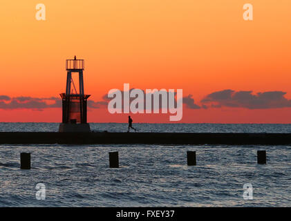 A man jogs past the North Avenue Beach lighthouse at sunrise in Chicago, Illinois, United States of America. Stock Photo