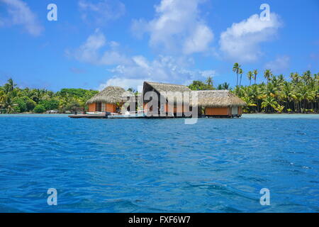 Tropical home with thatch roof over water with shore of an islet in background, Huahine island, Pacific ocean, French Polynesia Stock Photo