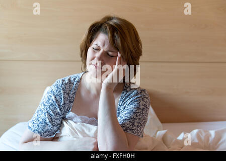 woman with a headache sitting on bed Stock Photo