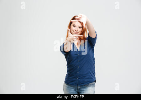 Happy attractive redhead young woman standing and making hands frame over white background Stock Photo