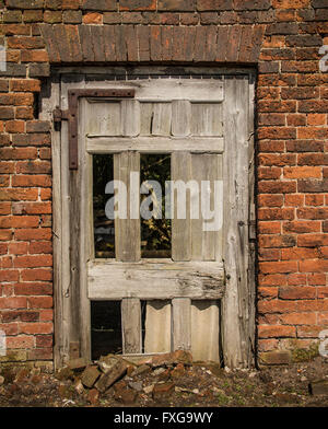 Broken door with missing panels, rusty hinge, old brickwork Stock Photo