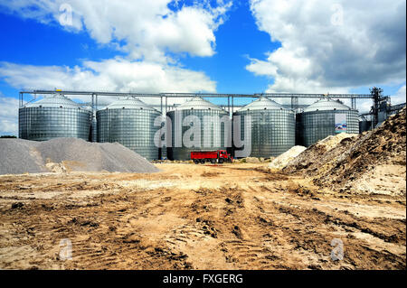 A row of granaries against the blue sky. Silos for wheat storage and drying. A red lorry in front of the granaries. Stock Photo