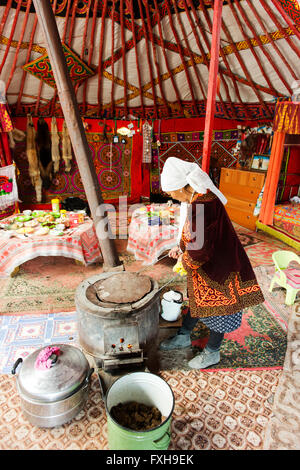 Kazakh woman in traditional dress attends the horse dung-fueled fire in her Ger. Stock Photo