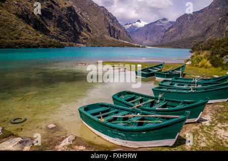 Huaraz, PERU in November 2015: Six green boats are waiting to be sailed across the blue glacier lagoon in the Peruvian Andes. Hu Stock Photo