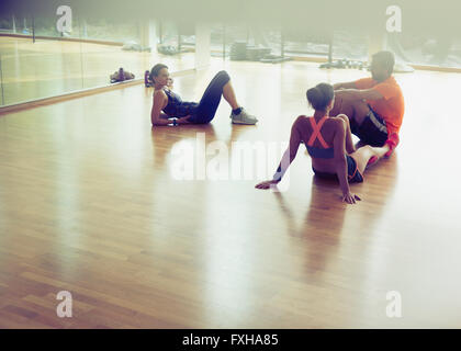 Friends resting and talking on gym studio floor Stock Photo
