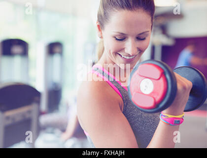 Close up smiling woman doing dumbbell biceps curls at gym Stock Photo