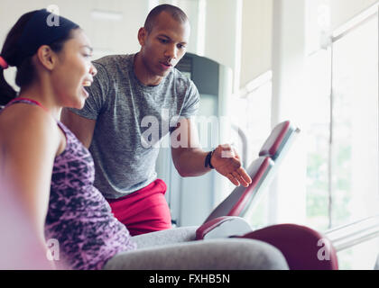 Personal trainer guiding woman on exercise equipment at gym Stock Photo