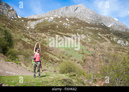 brunette sport hiker or trekking woman with red shirt green trousers stretching her arms to rest down mountain in Picos de Europ Stock Photo