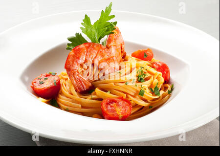 Single bowl serving of spaghetti noodles and prawns on top surrounded by sliced cherry tomato and parsley Stock Photo