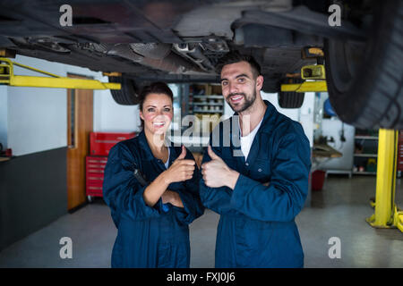 Mechanics giving thumbs up standing under a car Stock Photo
