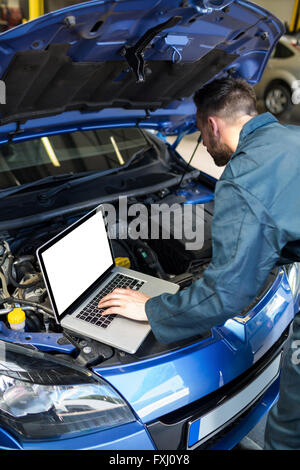 Mechanic examining car engine with help of laptop Stock Photo