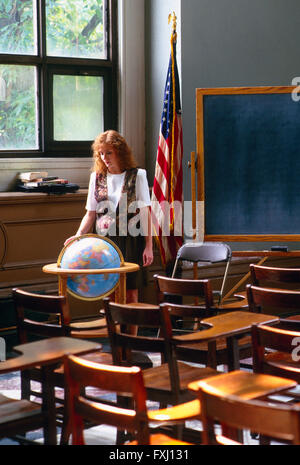 Female red headed teacher in classroom with world globe, American Flag & chalk board Stock Photo