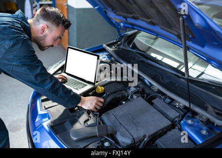 Mechanic examining car engine with help of laptop Stock Photo