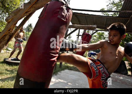 Kids training at improvised muay thai training center. A boy kicks the sand bag. Stock Photo